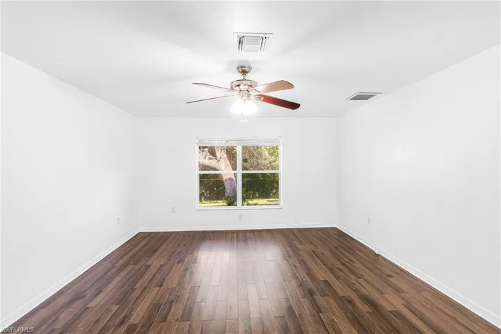 Room featuring wood-finish flooring, white walls, a multi-pane window, and a ceiling fan with integrated lighting