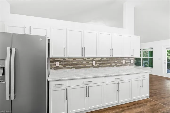 Kitchen featuring white shaker cabinetry, an elongated mosaic tile backsplash, light-toned countertops, and wood-finish flooring