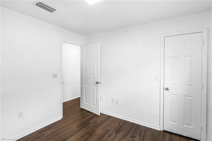 Room featuring wood-finish flooring, white painted walls, white baseboards, and white six-panel doors