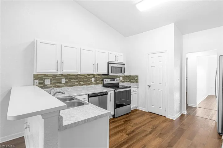 Kitchen featuring white cabinetry, wood-finish flooring, stainless steel appliances, a breakfast bar, and a mosaic tile backsplash