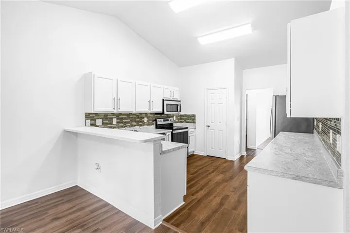 Kitchen featuring vaulted ceilings, wood-finish flooring, white cabinetry, a mosaic tile backsplash, and stainless steel appliances