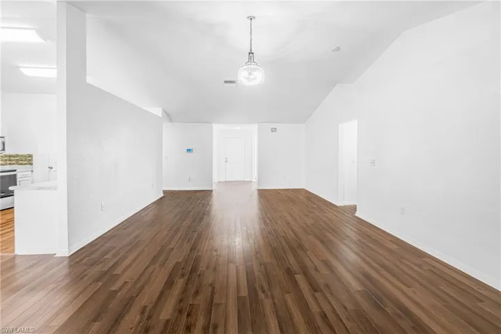 Spacious interior featuring wood-finish flooring, vaulted ceilings, and a modern pendant light fixture