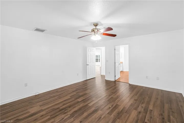 Spacious room featuring wood-finish flooring, white painted walls, a ceiling fan with integrated lighting, and two interior doorways