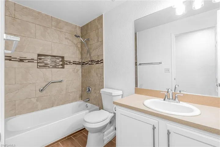 Bathroom featuring a white bathtub, ceramic tile surround with mosaic accent, built-in shower niche, and a vanity with an integrated sink and light-toned countertop