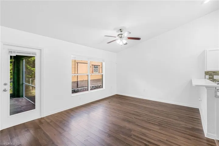 Bright open-concept living area featuring wood-finish flooring, a contemporary ceiling fan, and crisp white walls