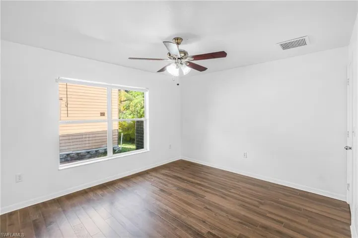Spacious room featuring wood-finish flooring, a large window, a ceiling fan with integrated lighting, and white baseboards