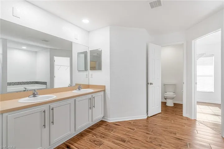 Bathroom featuring a dual vanity with a beige countertop, white cabinetry, and wood-look tile flooring