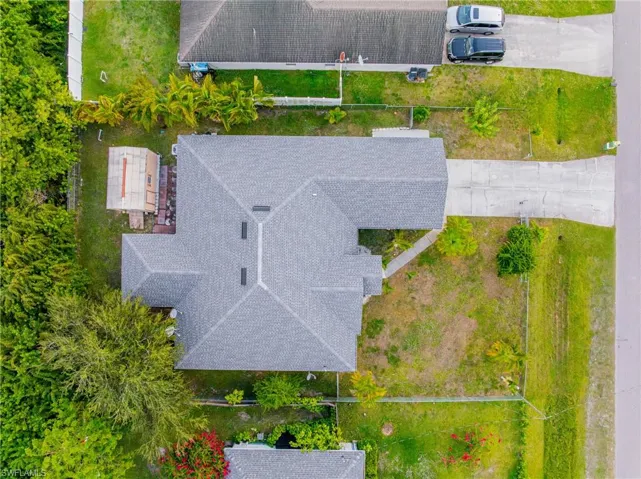 Aerial view of the property featuring a gray shingle roof, a paved driveway, and established perimeter trees