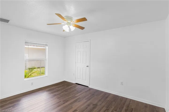 Room featuring wood-finish flooring, a ceiling fan with integrated lighting, and a white paneled door