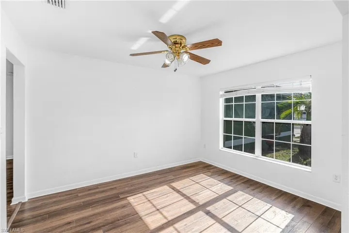Bright interior space featuring wood-finish flooring, a multi-pane window, and a ceiling fan with integrated lighting