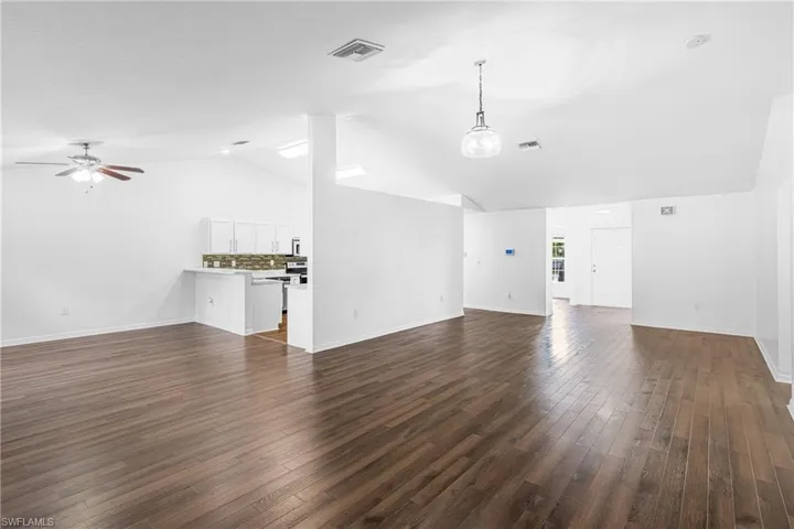 Open-concept living space featuring wood-finish flooring, vaulted ceilings, and white wall finishes