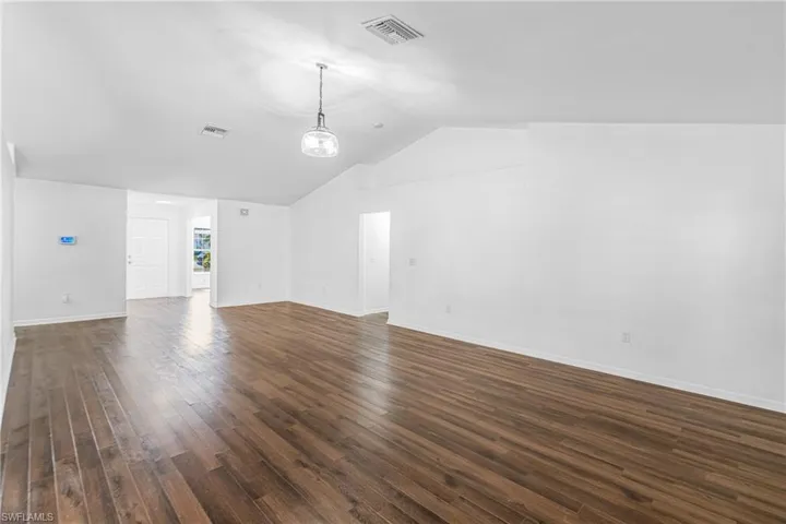 Spacious room featuring vaulted ceilings, wood-finish flooring, a modern pendant light fixture, and white painted walls