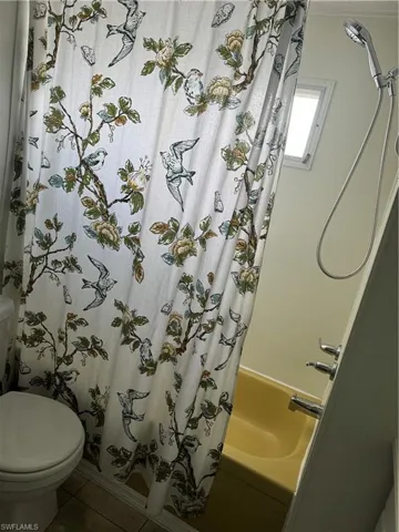 Bathroom with tile patterned floors, shower / bath combo, and toilet