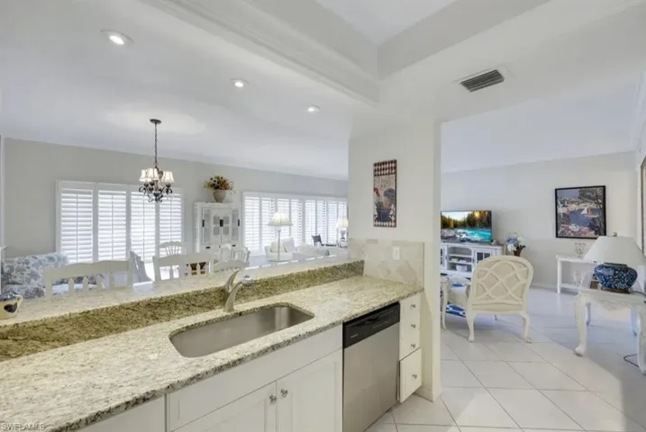 Kitchen with dishwasher, a sink, a chandelier, light stone counters, and recessed lighting