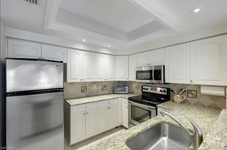Kitchen with appliances with stainless steel finishes, a sink, light stone counters, white cabinets, and recessed lighting