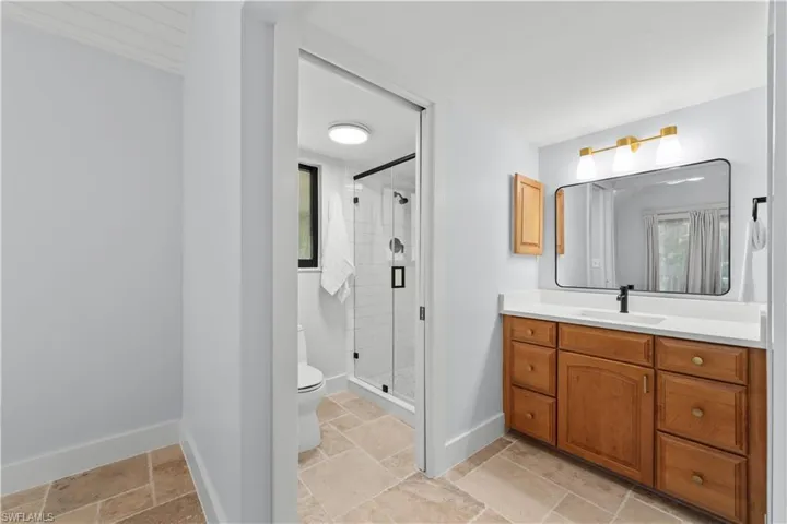 Full bath with toilet, vanity, a shower stall, baseboards, and stone tile floors