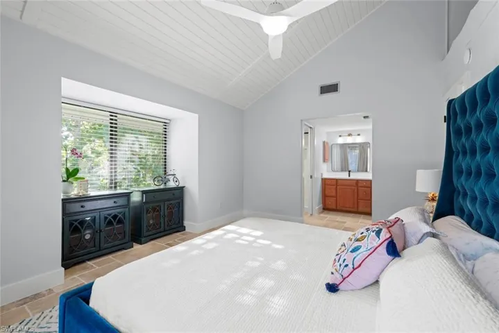 Bedroom featuring connected bathroom, light tile patterned flooring, baseboards, and high vaulted ceiling
