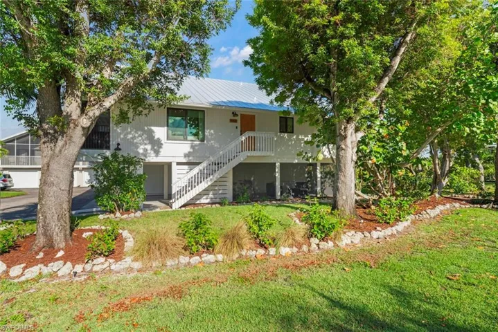 Coastal inspired home featuring stairs, metal roof, and a front lawn