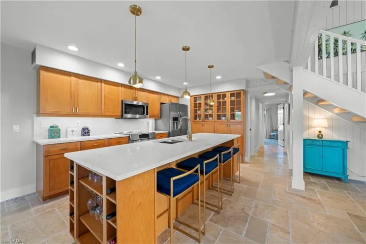Kitchen featuring stone tile flooring, appliances with stainless steel finishes, recessed lighting, light countertops, and an island with sink