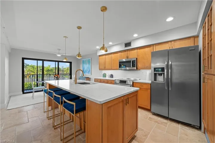 Kitchen featuring appliances with stainless steel finishes, a sink, stone tile flooring, recessed lighting, and an island with sink