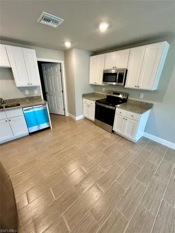 Kitchen with white cabinetry, stainless steel appliances, dark stone counters, and wood tiled floors