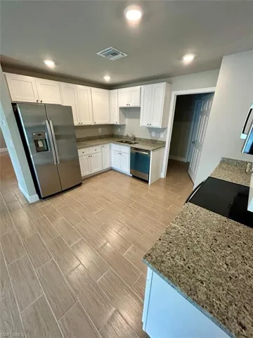Kitchen featuring stainless steel appliances, light stone counters, white cabinetry, wood tiled floors, and recessed lighting