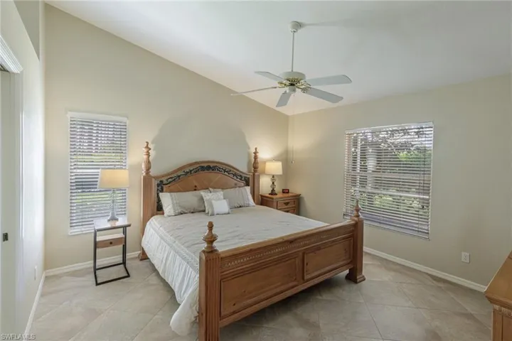Bedroom featuring vaulted ceiling, multiple windows, light tile patterned floors, and ceiling fan
