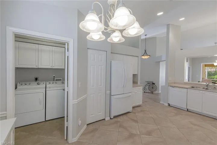 Kitchen with washing machine and clothes dryer, a chandelier, white appliances, white cabinets, and a towering ceiling