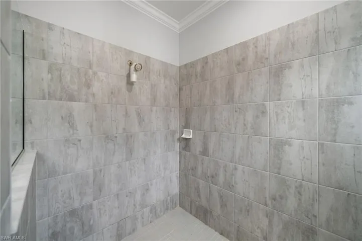 Bathroom featuring a tile shower and crown molding