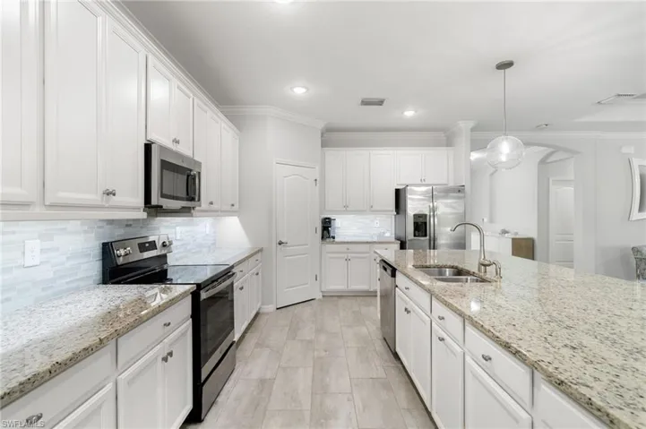Kitchen featuring pendant lighting, backsplash, stainless steel appliances, sink, and white cabinets