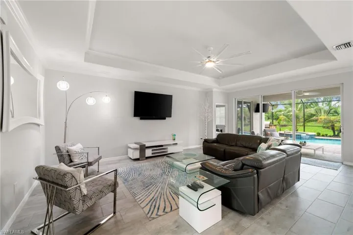 Living room with ceiling fan, a raised ceiling, and crown molding