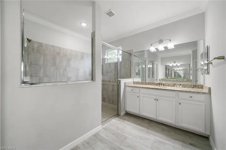 Bathroom with tiled shower, ornamental molding, and vanity