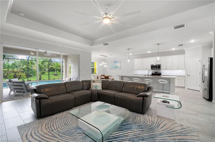 Living room with a tray ceiling, ceiling fan with notable chandelier, crown molding, and sink
