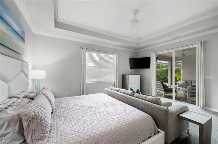 Carpeted bedroom featuring a raised ceiling, crown molding, and access to outside