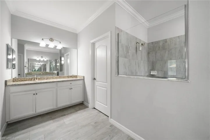 Bathroom with tiled shower, ornamental molding, and vanity