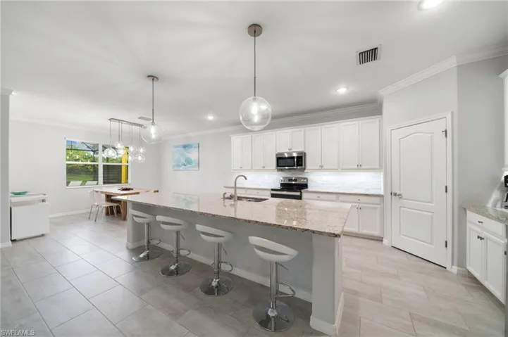 Kitchen featuring light stone countertops, appliances with stainless steel finishes, a kitchen island with sink, sink, and white cabinets