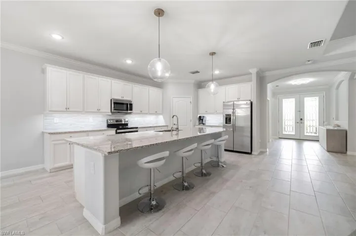 Kitchen with crown molding, appliances with stainless steel finishes, a center island with sink, and white cabinets