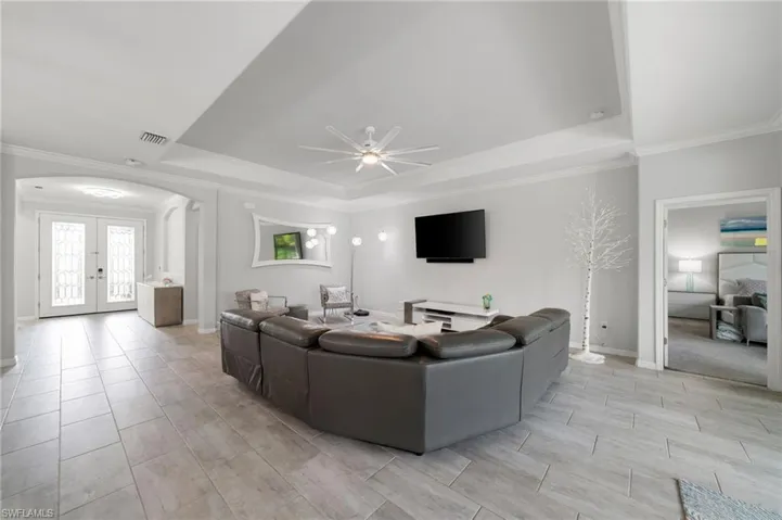 Living room with a tray ceiling, french doors, ornamental molding, and ceiling fan