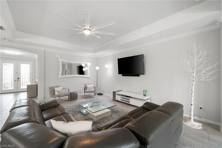 Living room with light wood-type flooring, a raised ceiling, ornamental molding, ceiling fan, and french doors