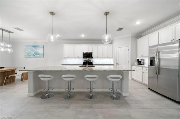 Kitchen with white cabinetry, an island with sink, stainless steel appliances, and a breakfast bar