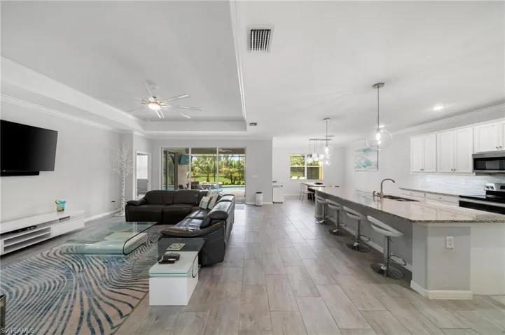 Living room with ceiling fan with notable chandelier, ornamental molding, light hardwood / wood-style flooring, sink, and a tray ceiling