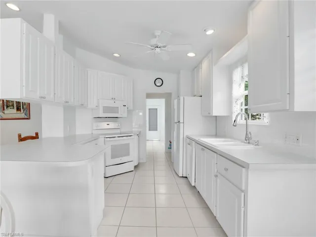 Kitchen with ceiling fan, sink, white appliances, and white cabinets