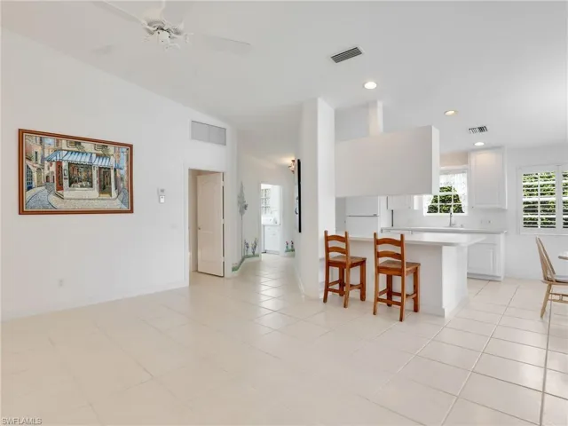Kitchen featuring lofted ceiling, white cabinets, a breakfast bar area, light tile patterned flooring, and white fridge