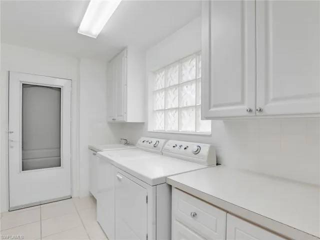 Clothes washing area featuring light tile patterned floors, sink, washer and clothes dryer, and cabinets