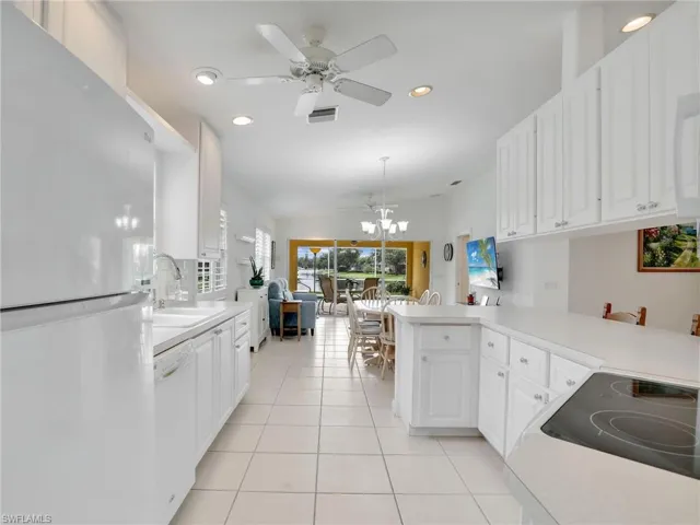 Kitchen with ceiling fan with notable chandelier, white cabinetry, kitchen peninsula, light tile patterned flooring, and white appliances
