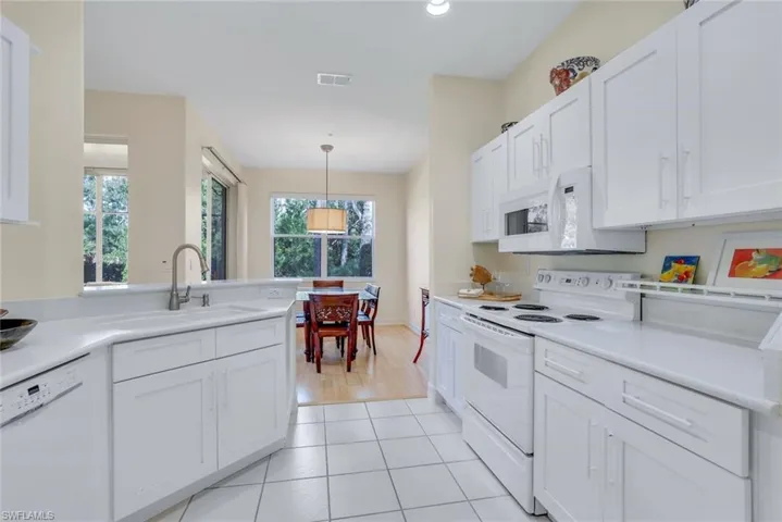Kitchen with hanging light fixtures, white cabinets, light tile patterned floors, sink, and white appliances