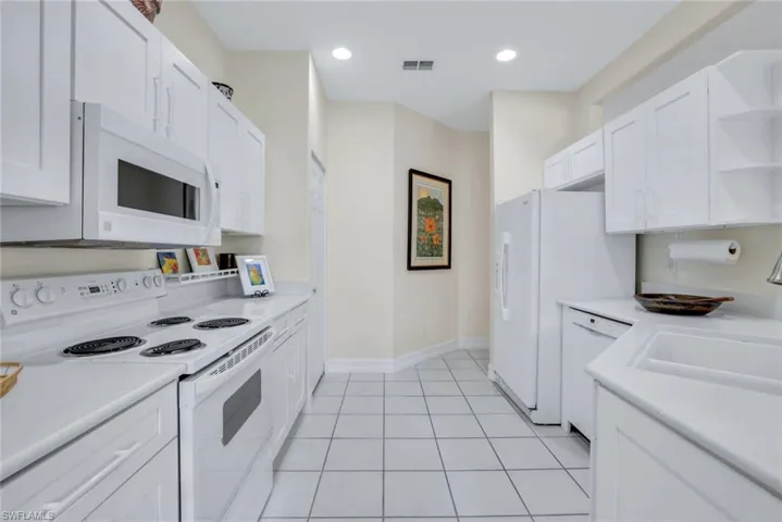 Kitchen with sink, white appliances, white cabinets, and light tile patterned floors