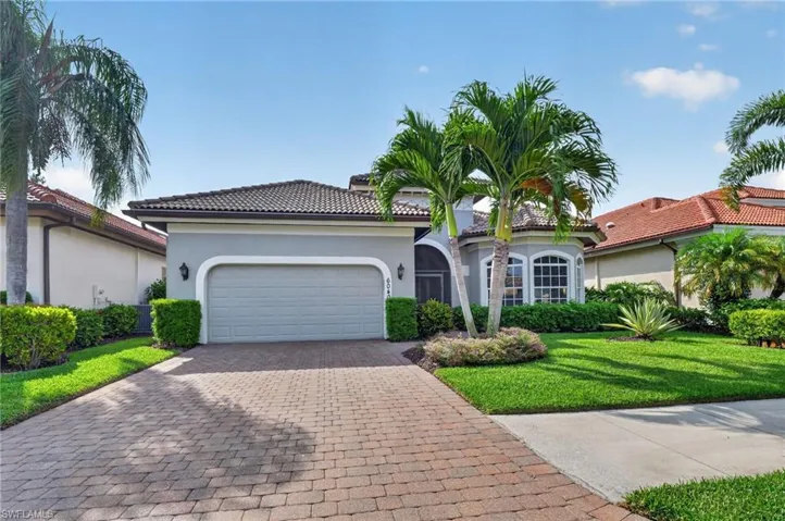 Stucco exterior with a tile roof, featuring a paver driveway, an arched garage door, and beautiful palm trees