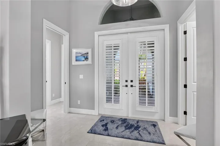 Double entry doors with interior plantation shutters, arched transom window, high ceilings, and tiled flooring
