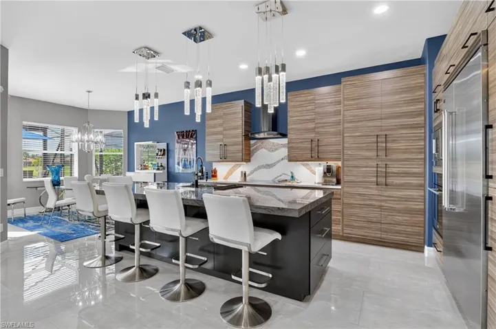 Modern kitchen featuring a large central island with wood-finish cabinetry, stainless steel appliances, a decorative backsplash, and polished tile flooring